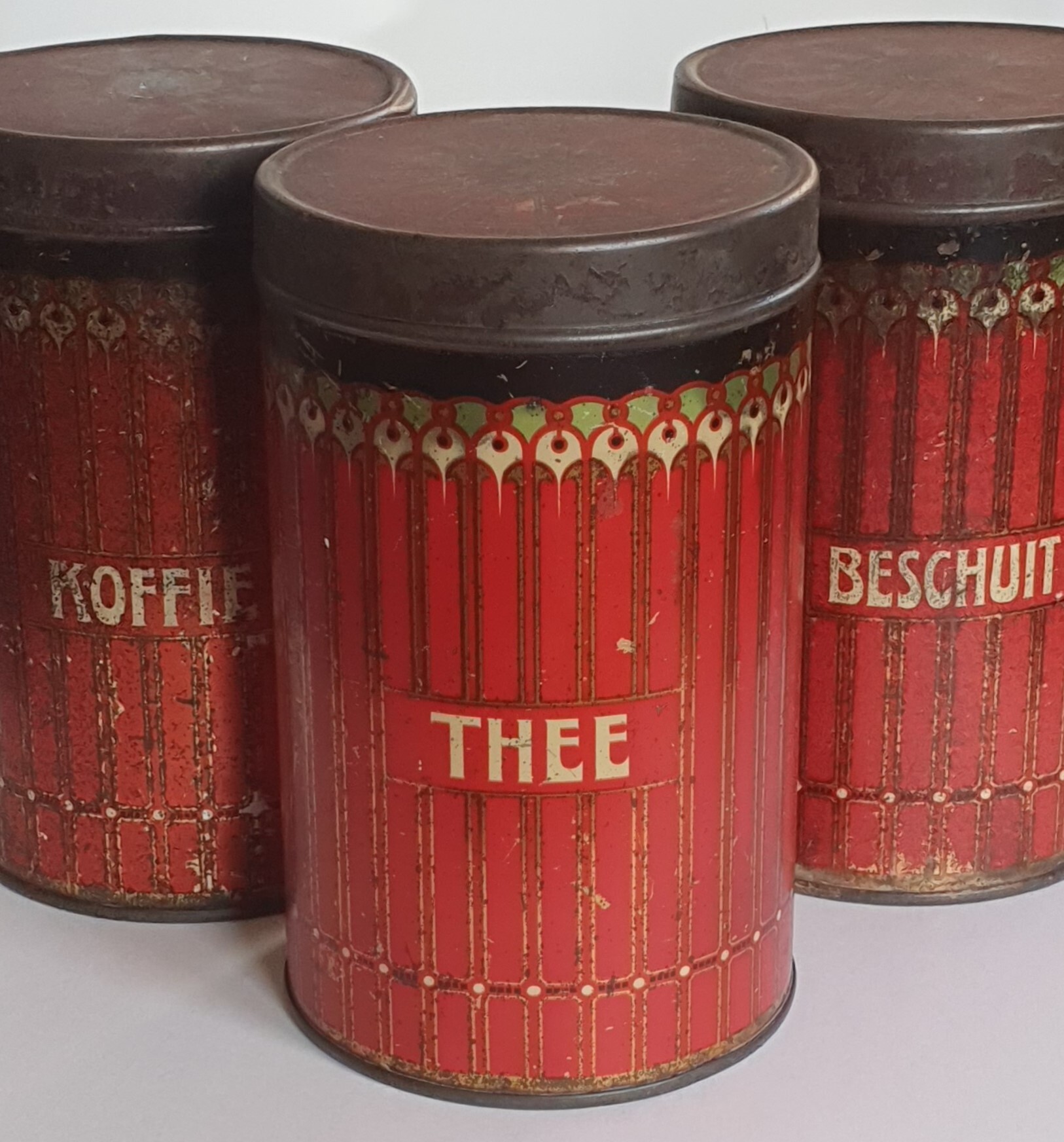 Drie rode merkloze voorraadblikken voor beschuit, koffie en thee.