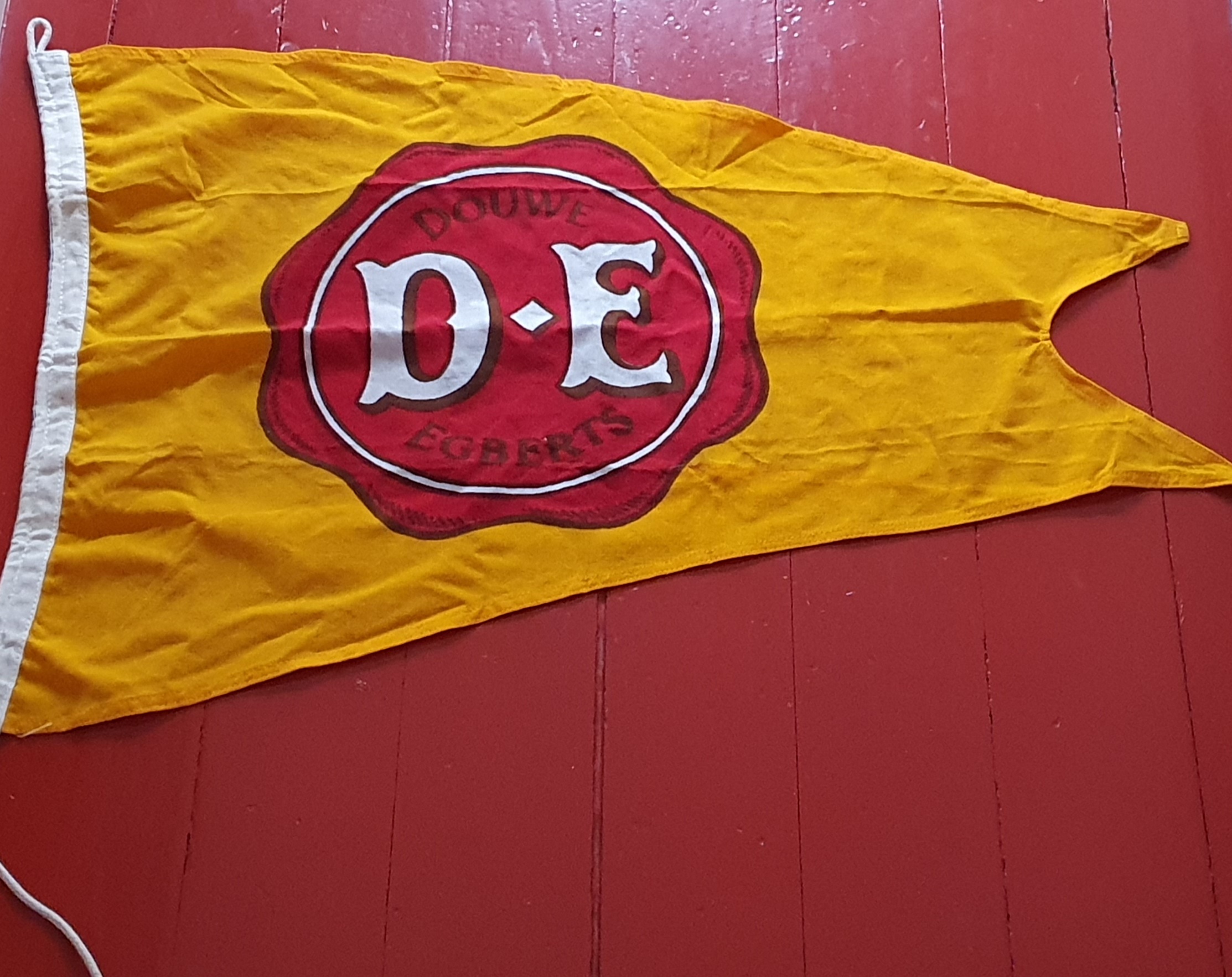 Douwe Egberts bedrijfsvlag, geel met het rode D.E. zegel.