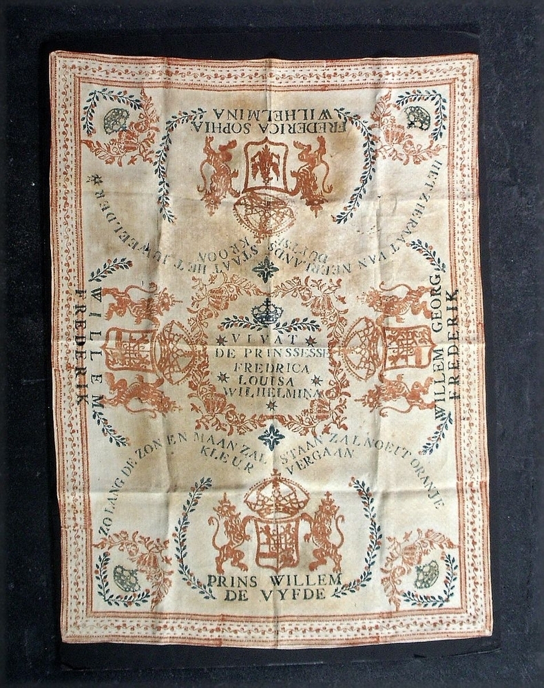 Doek, in de kleuren oranje/zwart/wit, met centraal een medaillon met een busteportret van de jonge Wilhelmina.