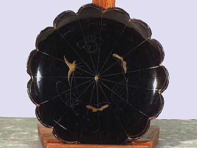 Ronde gelobde onderzetter van zwart gelakt dun hout; met vogeldécor in goud.