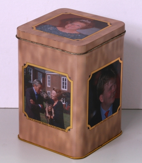 Rechthoekige trommel met scharnierend deksel. Kleur: gewolkt beige. Op zijvlakken en deksel in een goudkleurig kadertje afbeeldingen van koningin Beatrix, haar man en haar zonen.
