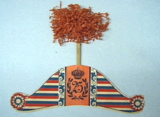 Feesthoedje in vorm van een steek, bekroond door een kartonnen stokje met oranje papierpluim.