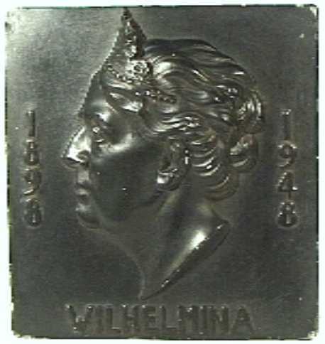 Tegel (gips of aardewerk) met naar voren springende portretkop van Wilhelmina naar links. Geheel is zwart geverfd.