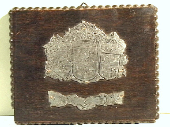 Houten plankje met daarop bevestigd en verzilverd wapenschild., met wapen van Juliana, Nederlandse koningswapen, en wapen van Bernhard.