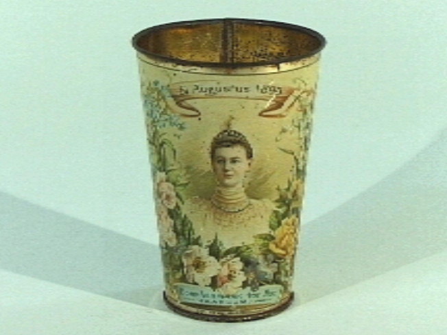 Blikken beker met afbeelding van de jonge koningin Wihelmina (busteportret), het monument 1813, het standbeeld van Laurens Jansz. Coster, en een bloemendecoratie.