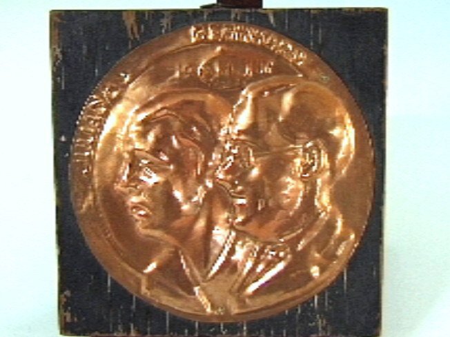 Rood koperen plaquette, rond, met busteportretten naar links van prinses Juliana en prins Bernhard.