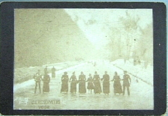 Foto van Koningin Wilhelmina op de schaats op een baan "GERESERVEERD VOOR H.M. DE KONINGIN", omstreeks 1890, op de gracht bij Huis ten Bosch. Op een rij met leden van de hofhouding.