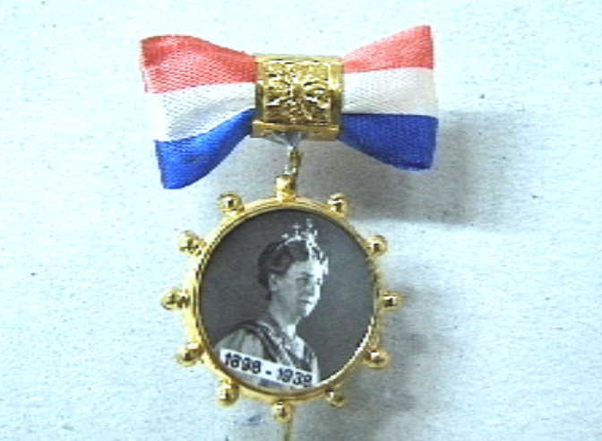 Steekspeldje met hangend aan een oogje een rond miniatuur fotoportret van koningin Wilhelmina en het opschrift 1898-1938.