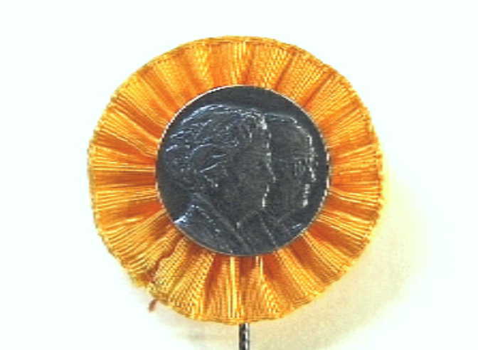 Speldje met busteportretten naar rechts van Juliana en Bernhard. Met oranje rozet.