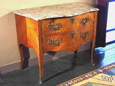 Buikvormige commode van rozehoutfineer op eikehout met twee laden en staande op hoge smalle poten.