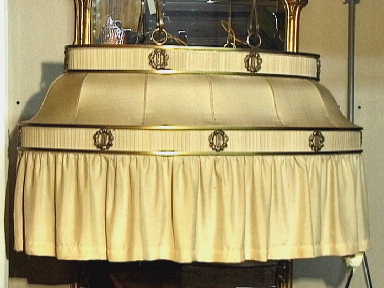 Grote ovale eettafellamp met gele stoffen kap aan vier gedraaide metalen beugels.