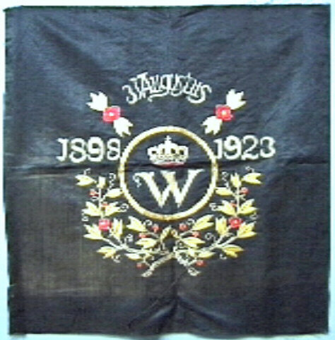Doek, zwart, met borduursel in goud, rood, geelgroen, en blauw. Centraal hoofdletter W met kroon erboven, omcirkeld in goud.