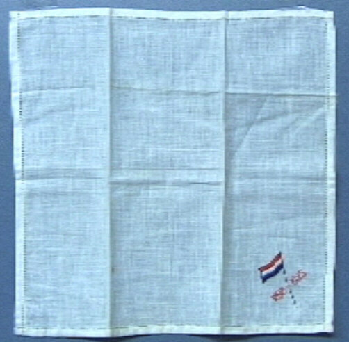 Zakdoekje, wit, omzoomd, met rechtsonder geborduurd een rood-wit-blauwe vlag en in rood "1898 - 1923".