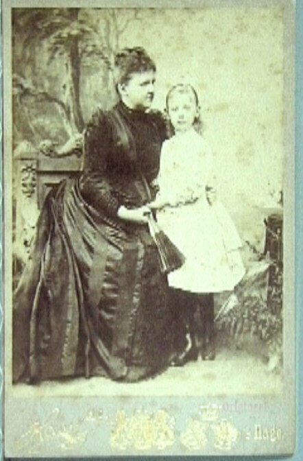 Foto van Koningin Emma zittend, in een donkere japon, met naast haar staand prinses Wilhelmina in een lichte jurk.