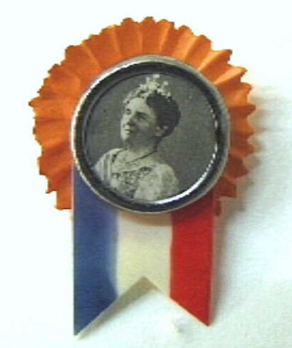 Rond speldje met fotoportretje van koningin Wilhelmina. Met oranje rozet en rood-wit-blauw vlaggetje.
