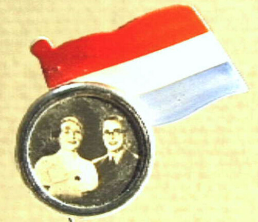 Rond speldje met busteportretten van Juliana en Bernhard, met een papieren driekleur.
