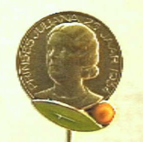 Rond speldje met busteportret naar links van Juliana, met aan de onderzijde een groen blad en een oranjeappel.