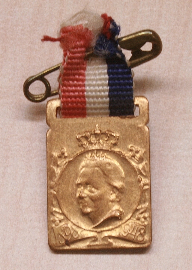 Rechthoekig insigne met in een cirkel een portret van koningin Wilhelmina naar links. Met rood-wit-blauw lintje.