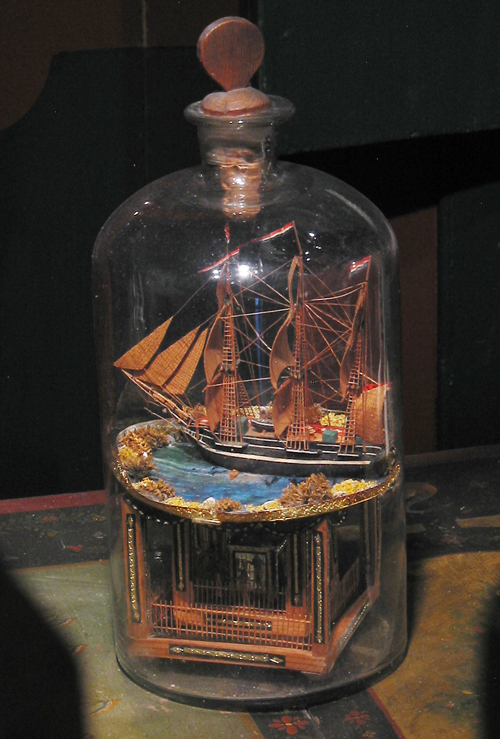 Schip in een fles. Miniatuur zeemansgraf in de vorm van een tempeltje met driemastbark in stolpfles, 19e eeuw