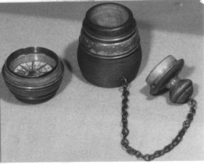 Gedraaid houten tondeldoos aan kettinkje met afschroefbare bodem, waarin een kompasje, cira 1800.