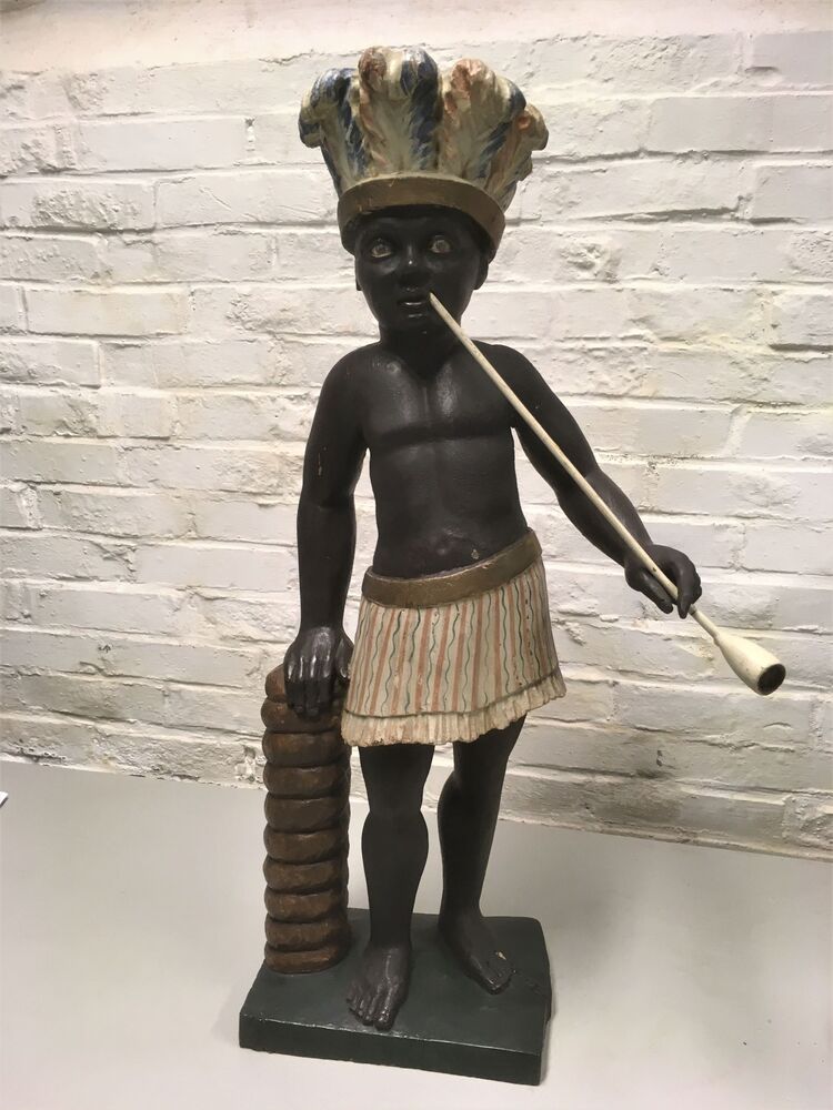 Houten beeld van een pijprokende donkere man met verentooi leunend op tabaksrol.