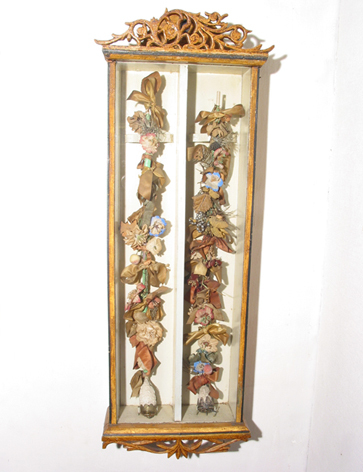 Twee aardewerken Friese of Drentse bruidegomspijpen, versierd met gedroogde bloemen, waarvan één met zilveren dop, in houten sierlijk bewerkt toonkast voor aan de wand