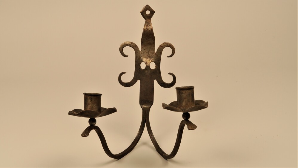 Metalen kandelaar voor twee kaarsen aan de muur.