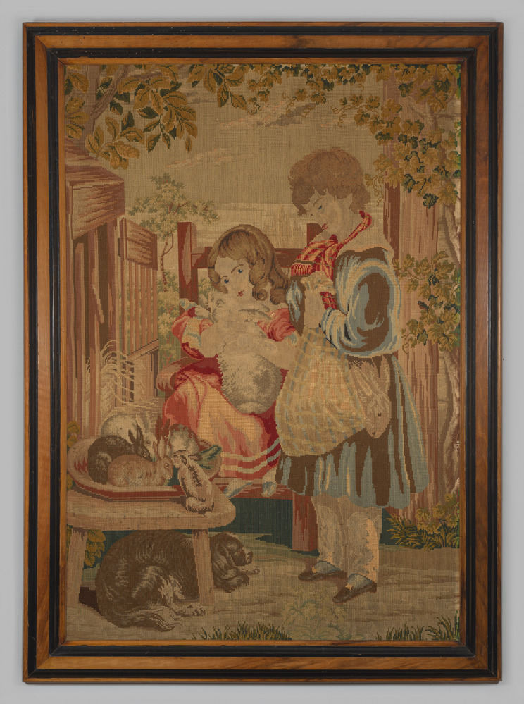 Borduurwerk, in lijst opgehangen, voorstellende een jongen, een meisje en een aantal konijnen.