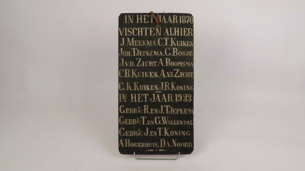 Zwart gelakt houten paneel met witte letters. Vermelding van de personen die in respectievelijk 1870 en 1933 op (onbenoemde) plek visten