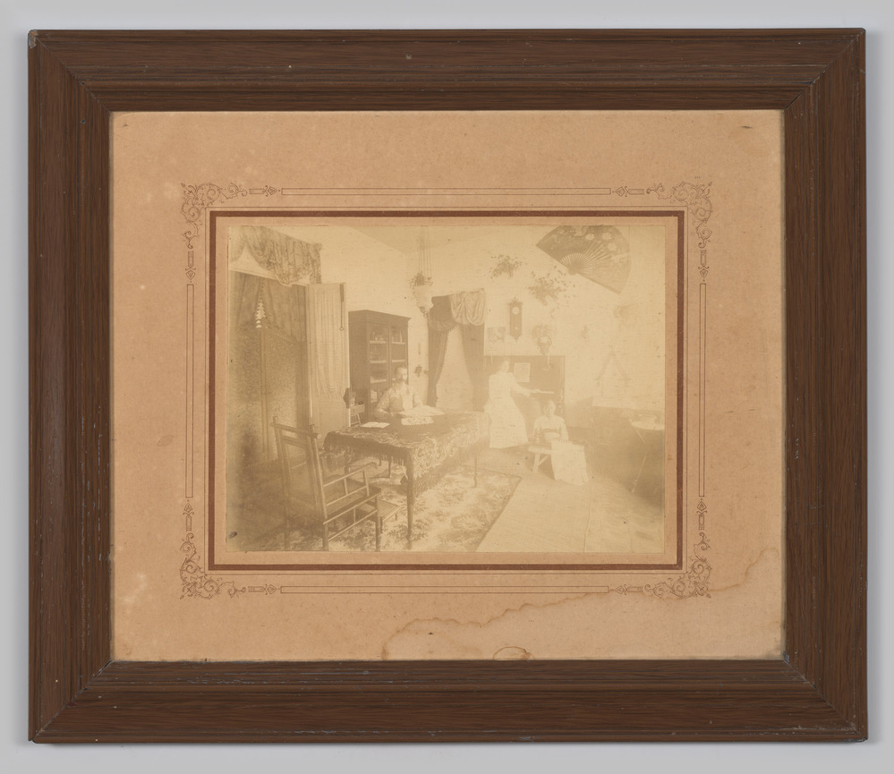 Foto, ingelijst, achter glas, enigszins vervaagd, voorstellende een man, een vrouw en een bediende.