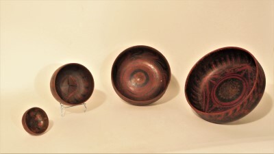 Houten schaaltje bruin gelakt met hierop zwarte en ossenbloedrode geometrische patronen, doorsnee 8,5 cm.