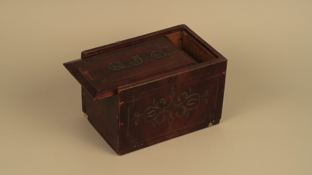 Houten kistje, rechthoekig met schuifdeksel, beschilderd: imitatie hout met daarop ornamenten in geel of goud, op deksel initialen G.J.E.