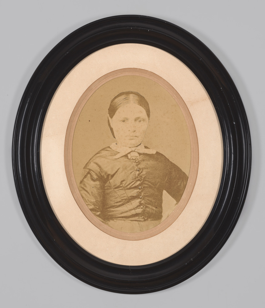 Reproductie van portretfoto, achter glas in ovale lijst, voorstellende een vrouw