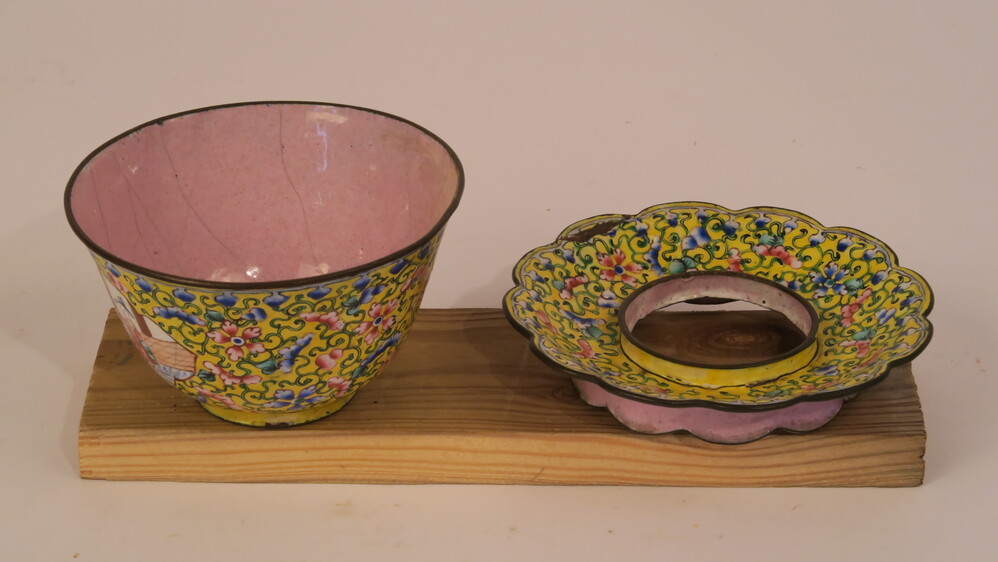 Uitbundig geglazuurde kom en schotel.I. kommetje zonder oor aardewerk met glazuur, chinees geinspireerde voorstelling met 2 vissers en 2 dames. Glazuur van florale motieven in blauw, roze en groen, op gele ondergrond. De binnenzijde van het kopje is roze geglazuurd. Sporen van reparatie. 
II. Metalen schoteltje met gat waarin het kopje past. Bovenzijde identieke florale motieven op gele ondergrond. Onderzijde identiek aan onderzijde kopje. Schoteltje met geschulpte rand.