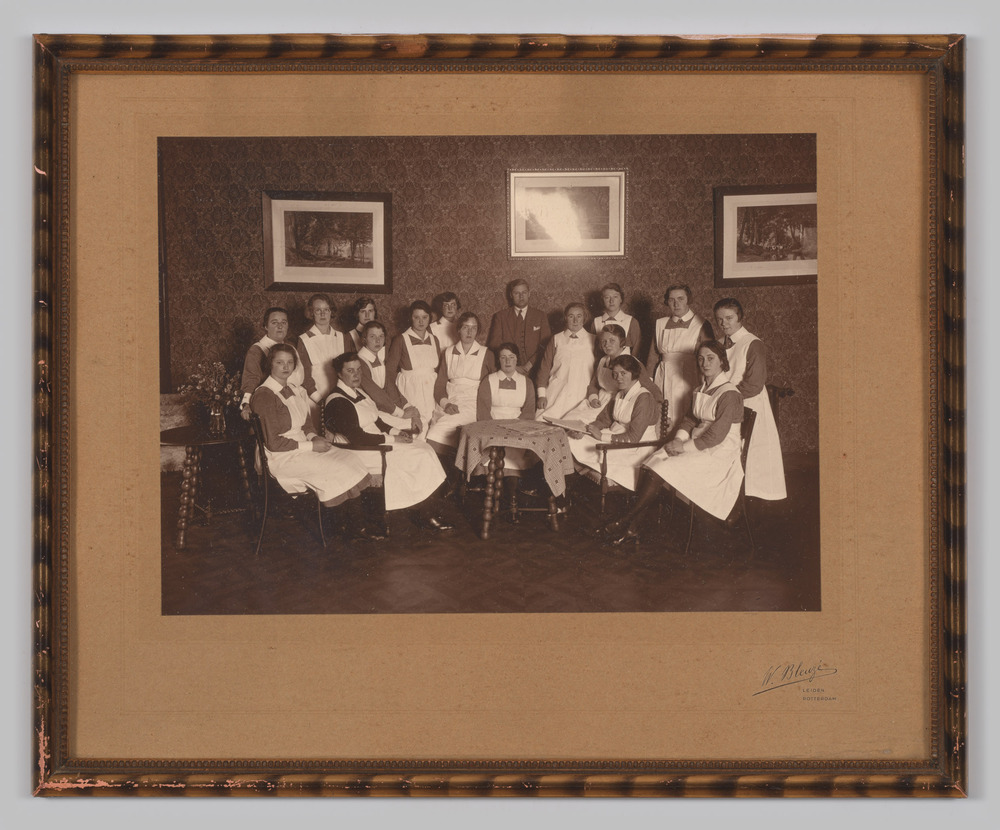 Groepsfoto, ingelijst, achter glas, van 17 vrouwen in verpleegstersuniform en 1 man