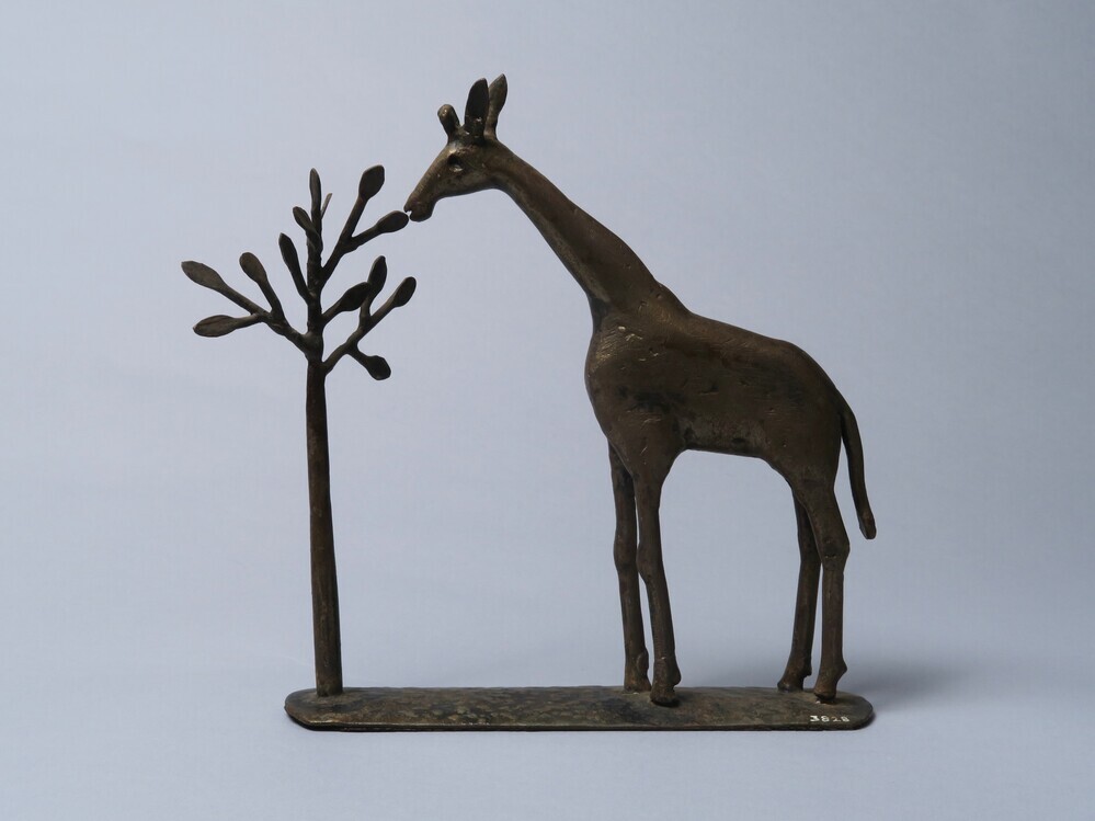 Metalen beeld van een giraffe bij een boom