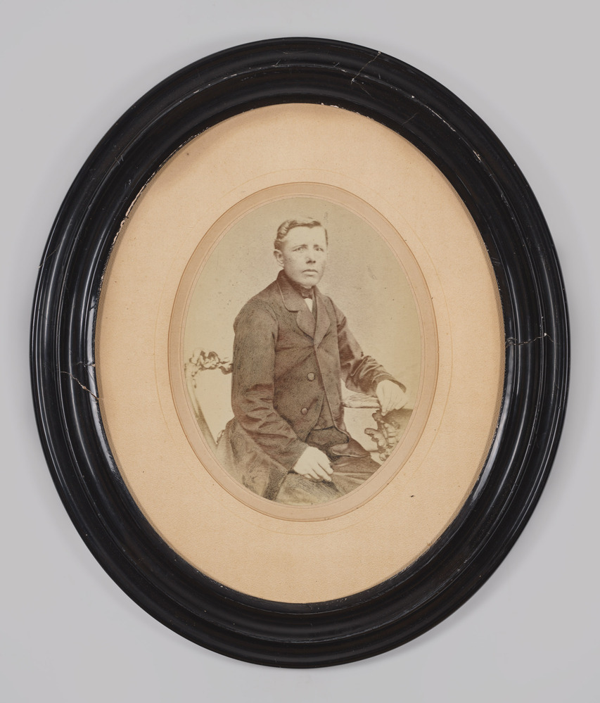 Portretfoto, achter glas, in zwarte ovale lijst, voorstellende een man
