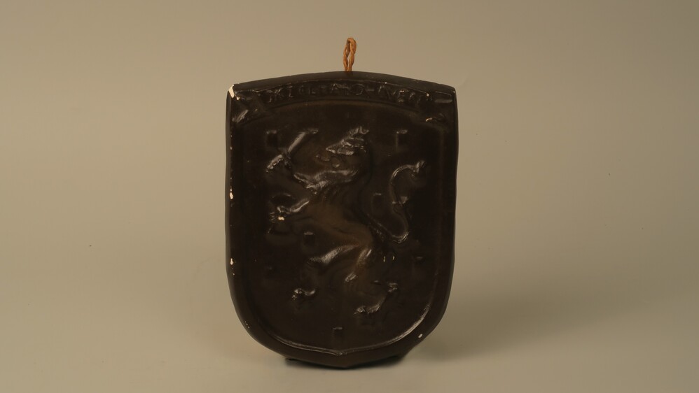 Wapenschild, donkerbruin, van gips, met de Nederlandse leeuw en de tekst "Ik zal handhaven"