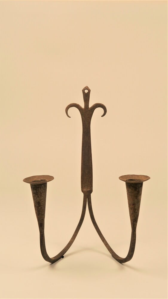 Metalen kandelaar voor twee kaarsen aan de muur.