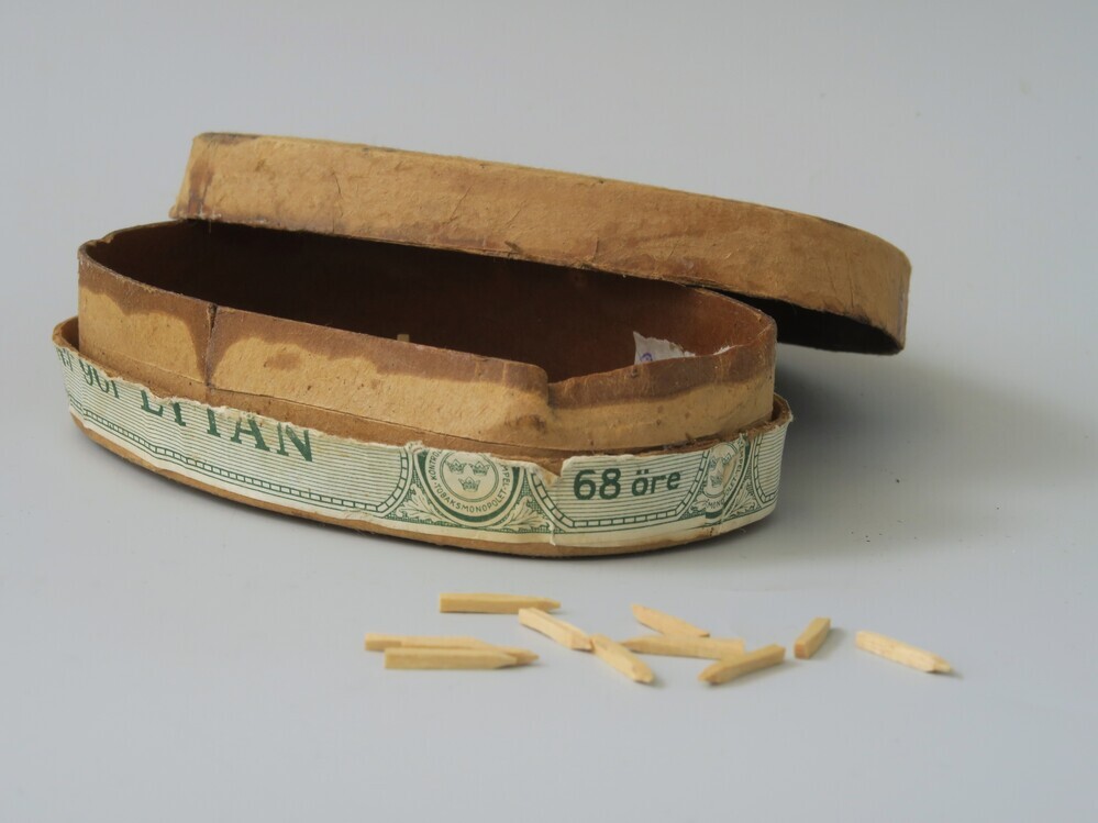 Houten nagels/spijkers (voor schoenmakers?) in een ovaalvormig tabaksdoosje met gescheurd etiket en merk op bovenkant deksel