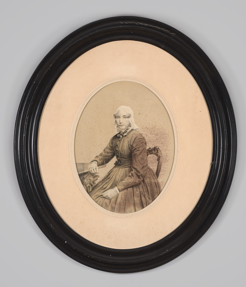 Portretfoto, achter glas, in ovale lijst, voorstellende een boerin