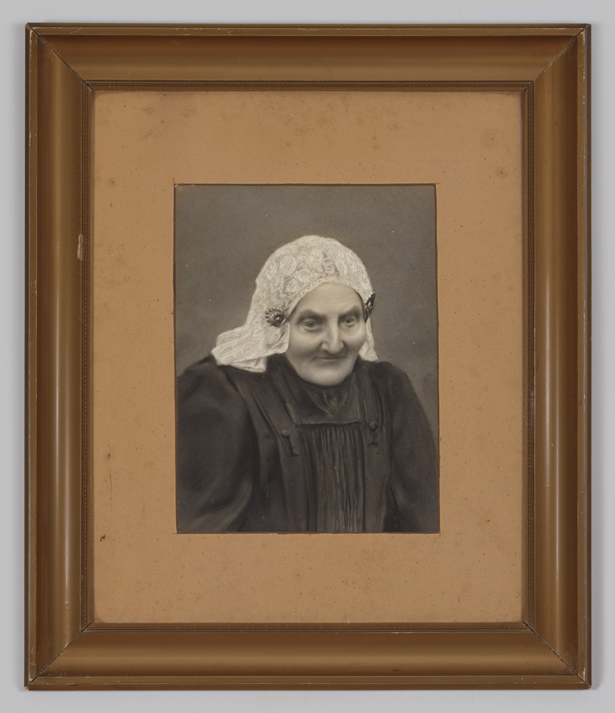 Ingelijst portret, achter glas, van een vrouw met witte floddermuts in zwarte jurk