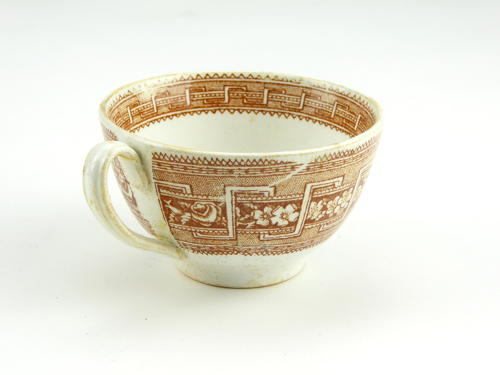 aardewerken kop van het merk Petrus Regout & Co, Maastricht, diameter 8,2 cm, op buitenkant bruine decoratie van bloemen en gestileerde wolfsangel, gemerkt met beeldmerk 71 A van Petrus Regout, opgedoken door British Sub Aqua Club, Branch 501, ook wel de 501 Divers uit Folkstone, uit het wrak van de op 19 november 1887 na een aanvaring met het stoomschip Rosa Mary gezonken stoomschip W.A. Scholten, via hun woordvoerder Glyn Jones geschonken aan het Veenkoloniaal Museum.