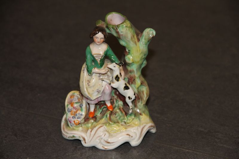 aardewerken beeldengroep van vrouw naast een boom, naast haar een staande gevlekte hond met zijn voorpoten op haar schoot.