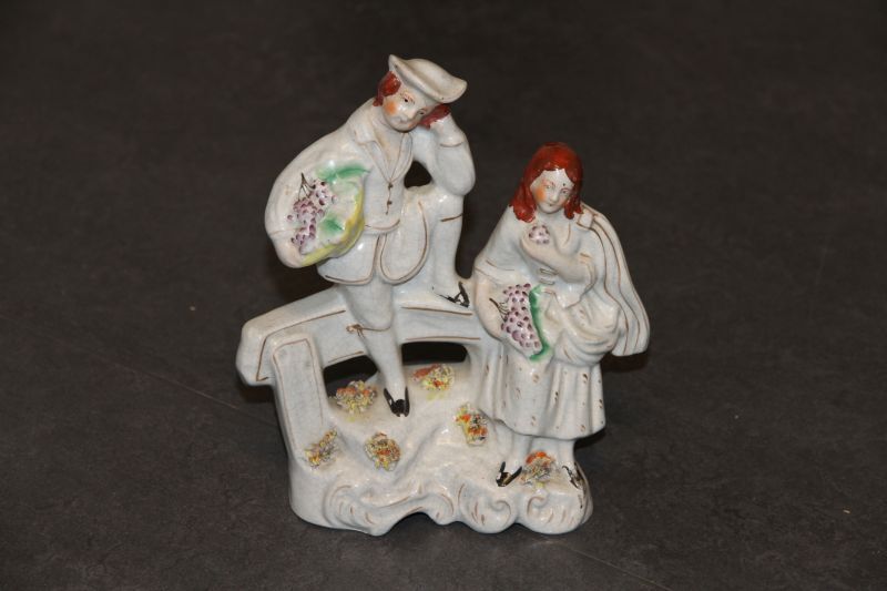 Victoriaans beeldje van een man en een vrouw met druiven, leunend tegen een balk