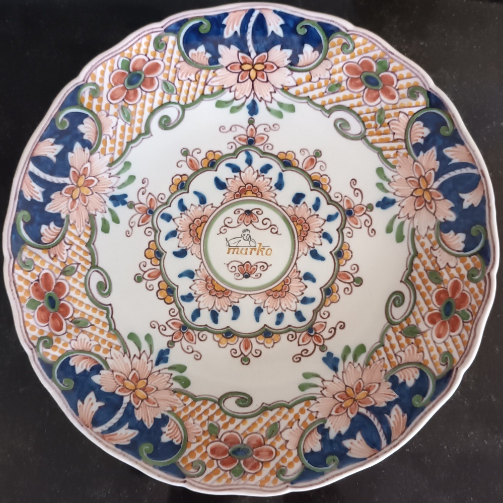 Ronde aardewerken bord met achterop bruine stempel Koninklijke Tichelaar Makkum, met roodkoperen ophangsysteem aan achterkant, voorkant rand bloemdecoraties waarin cartouche van bloemdecoraties en groene sierlijn een cirkel met boven en onder een bloemknop, daartussenin logo Marko Schoolmeubelenfabriek Veendam, een kinderhoofd en halve lichaam boven bruine belettering Marko. Afkomstig van T.J.Siepel (1917-2002), vader van schenkster. Hij is begonnen in Kootstertille tot eind 1954 en heeft tot halverwege de 70-er jaren bij Marko gewerkt, samen met de heren Kooistra, enz. Daarna eigen bedrijf opgestart in Wildervank (achter Wortman) en later samengegaan met het bedrijf van dhr. J. de Bruin, Borgerspark 152 in Veendam wat resulteerde in 'Metaalindustrie Veendam B.V.'
( nog steeds aktief aan De Zwaaikom ). Hij woonde aan de Wilhelminasingel 5 in Veendam.