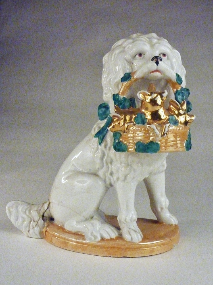 witte zittende steengoed poedel met okerkleurige mand vol goudkleurige biggetjes met erachter groene blaadjes, Duits aardewerk, maar in de stijl van Staffordshire.