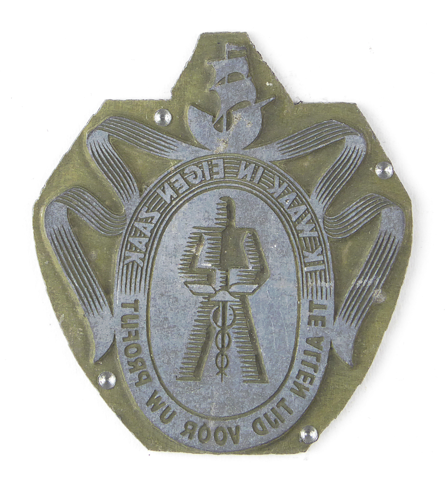 ietwat ovale non ferro metalen cliche met rechthoekige bovenstukje, met afbeelding ovaal met hierin harnas die esculaapvormige zwaard vasthoud, boven rondom banier met op de top een zeilschip, rondschrift om ovaal ik waak in eigen zaak te allen tijd voor uw profijt ( wapenspreuk van de Stichting Reclame Middenstand), afkomstig van kantoorinstallaties Bv Schuur te Veendam