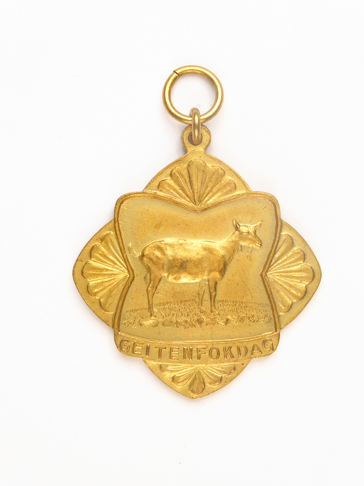 metalen goudkleurige medaille, 8 hoekig met afgeronde hoeken, voorkant klaverbladvormig, aan vierkanten schelpvormige hoeken, aan voorkant afbeelding van een geit en inscriptie geitenfokdag, achterkant inscriptie prov k 5-9-59 1E 2j V bl 5929 RvJ H Dijkstra