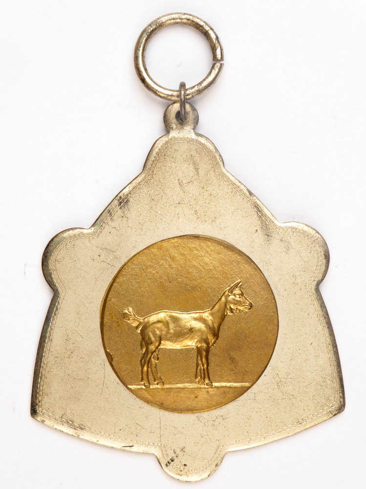 zilverkleurige medaille met koperen middencirkel met afbeelding van een geit en op achterkant inscriptie 1e pr S 887